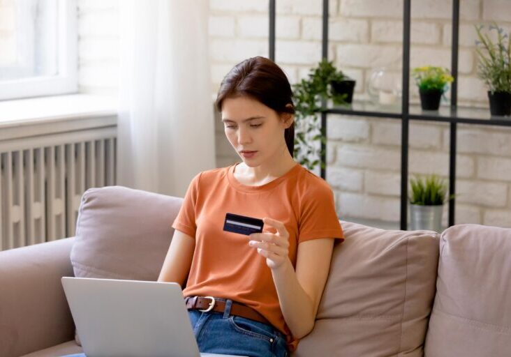 Young brunette woman looking at credit card with laptop in her lap